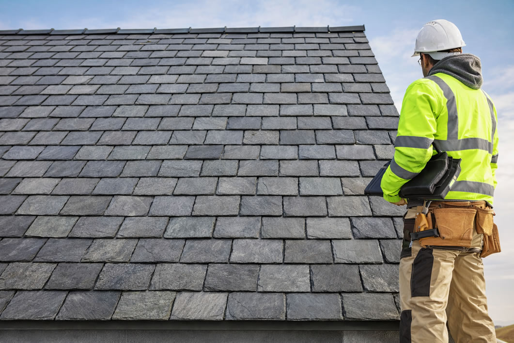 roofing uk - roofer inspecting newly installed roof with natural slate material